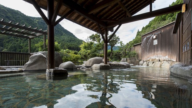Un bain traditionnel en bois, doté d’une piscine en pierre, de poutres en bois et surplombant un paysage montagneux.