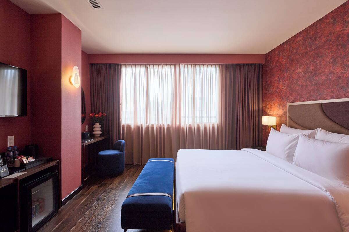 A hotel room with a large bed, a desk with a computer, a chair, and a window with curtains.