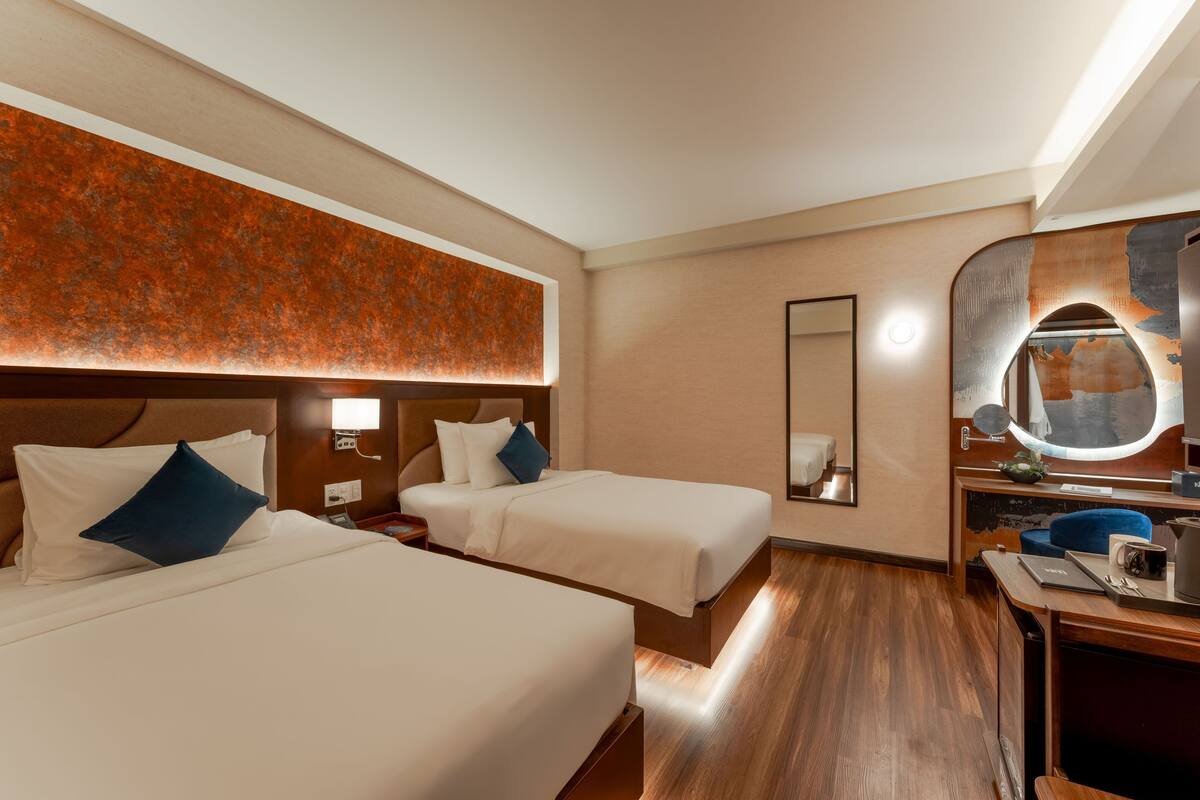 A hotel room with two beds, a desk, a mirror, and a wall with a textured design.