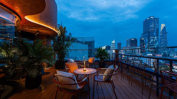Terraço no telhado com áreas de estar, plantas em vasos e vista para a paisagem urbana.