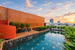 A rooftop pool with a city skyline view, surrounded by potted plants and a modern architectural design. - KiN Hotel Ly Tu Trong Edition (Ho Chi Minh City)