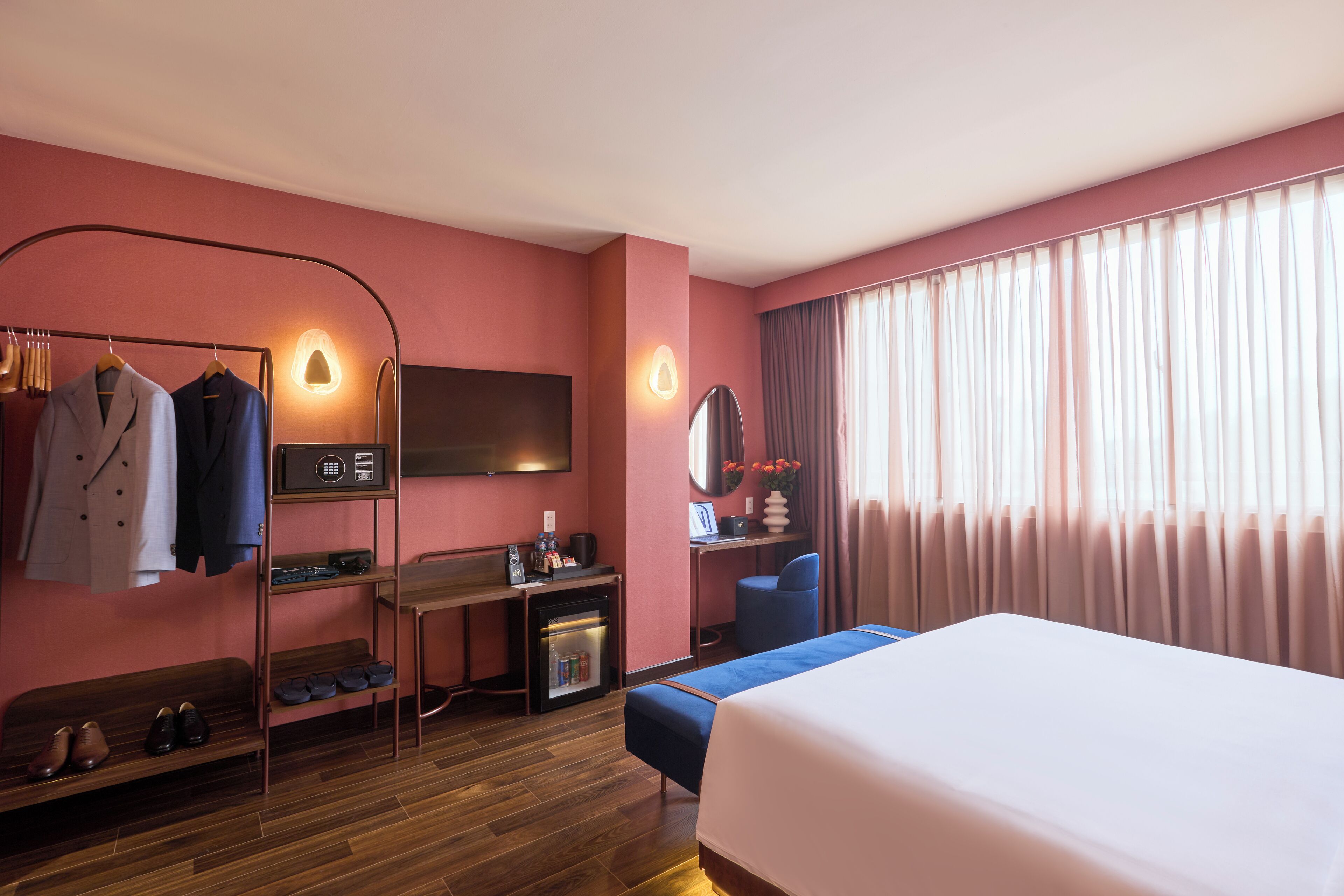 A hotel room with a bed, a desk with a chair, a wardrobe, a TV, and a window with curtains.