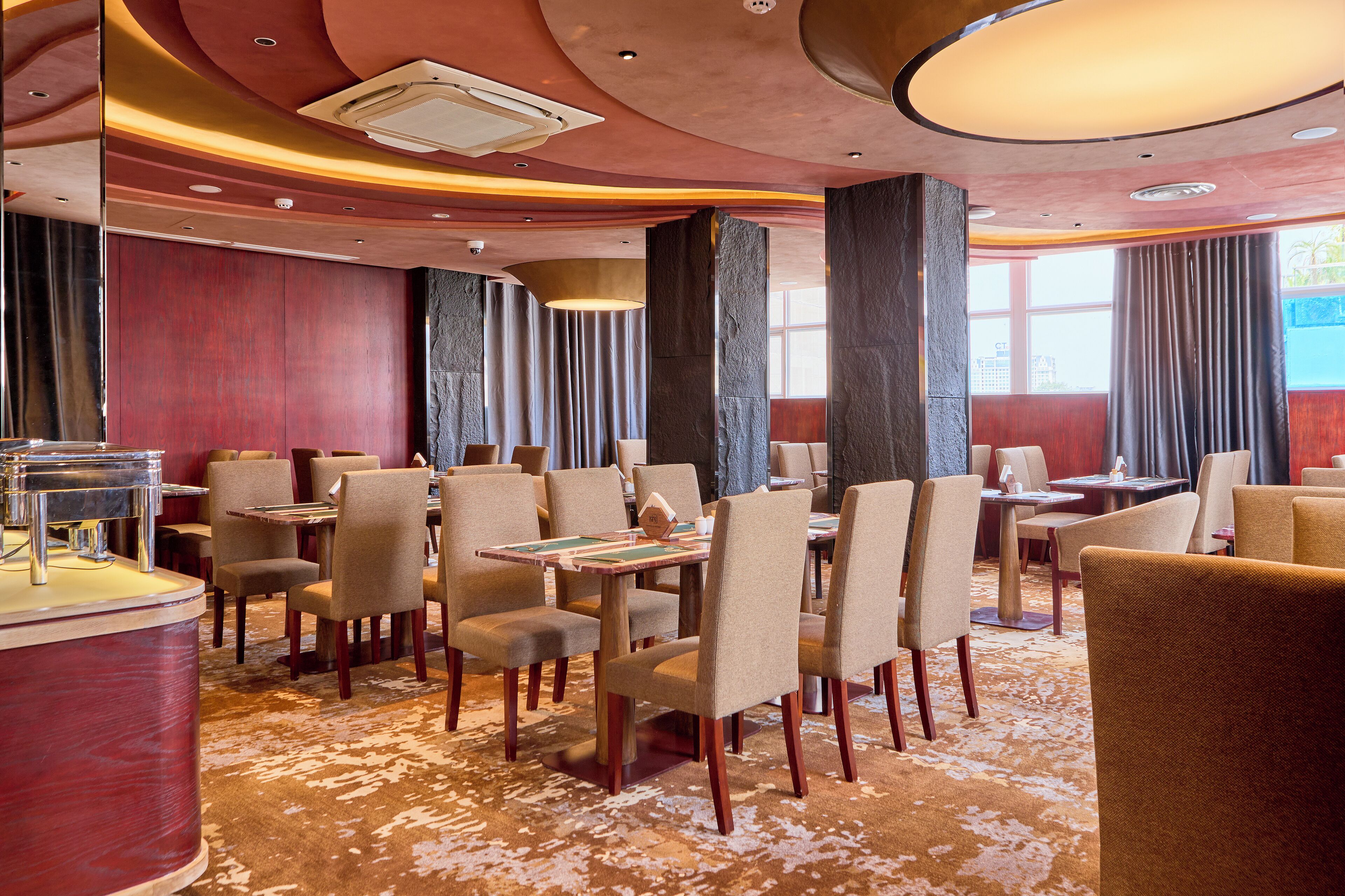 Une salle à manger d’hôtel avec de nombreuses tables et chaises, un système de climatisation central et une vue sur l’extérieur grâce à de grandes fenêtres.
