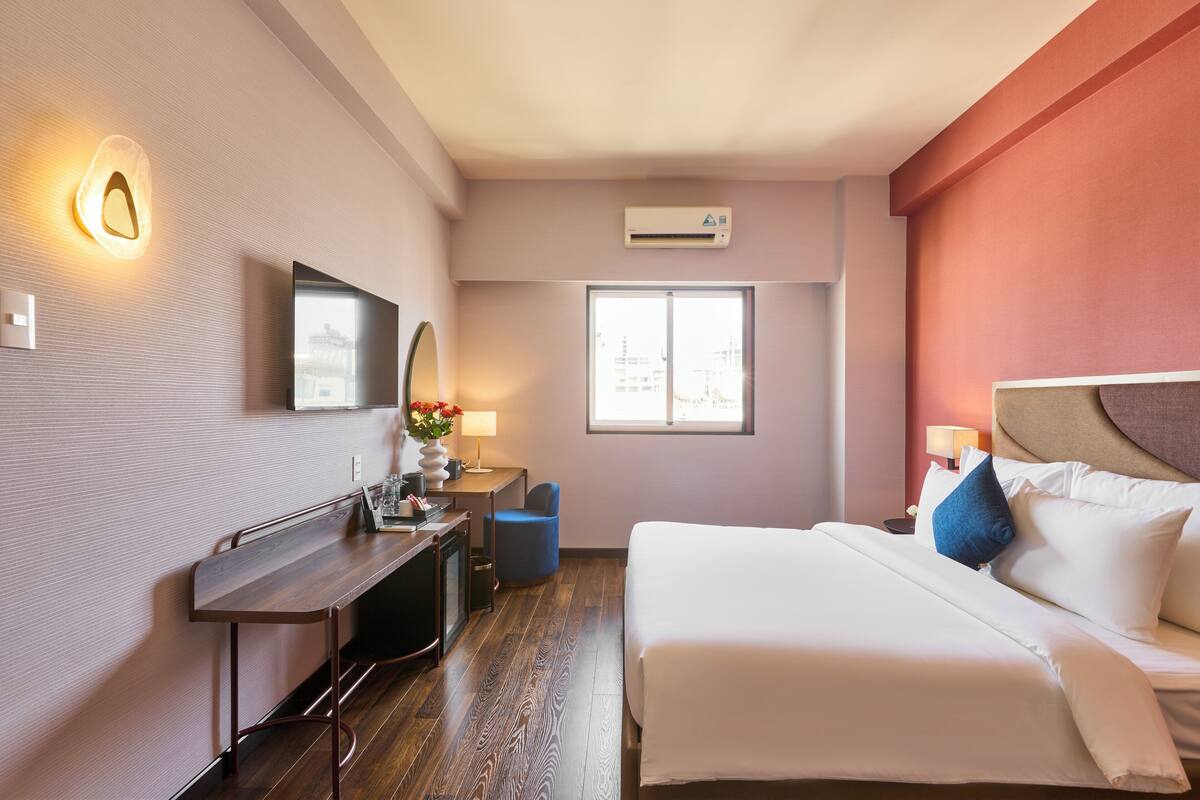 A hotel room with a bed, desk, chair, and a window with a city view.