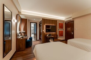 A hotel room with a large bed, a desk with a chair, a TV, a mirror, and a door.