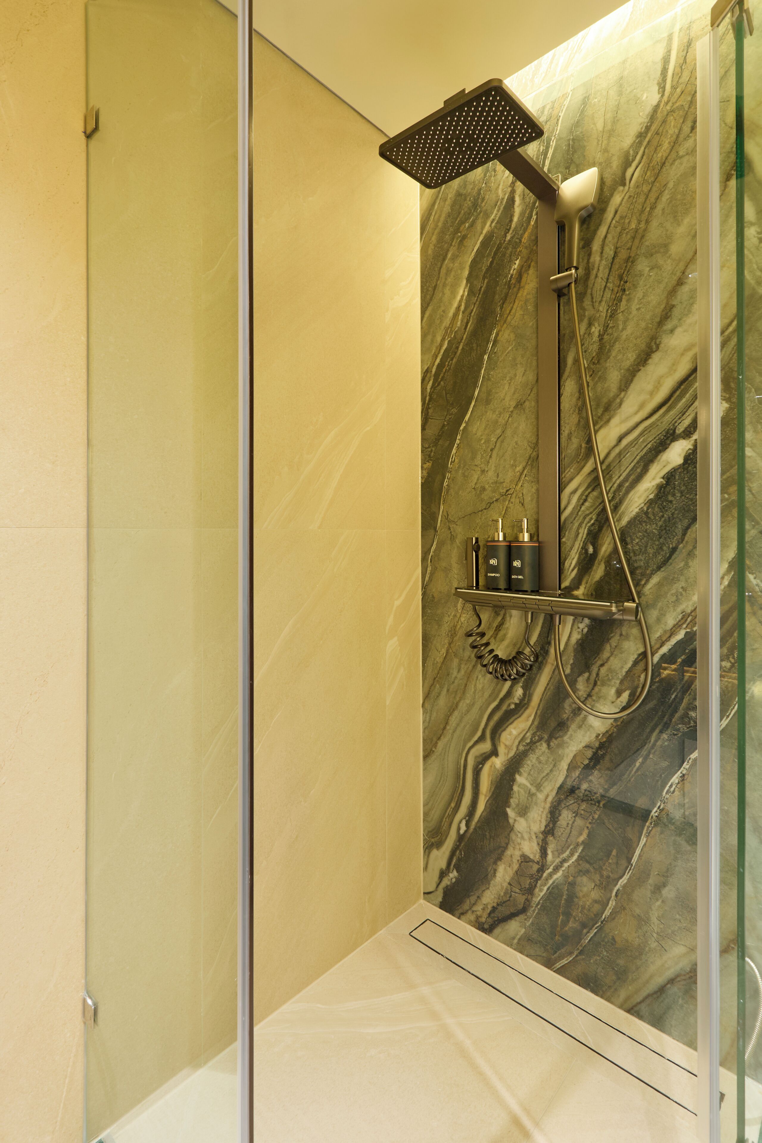 A modern bathroom with a marble wall, a glass shower enclosure, and a built-in shelf with toiletries.