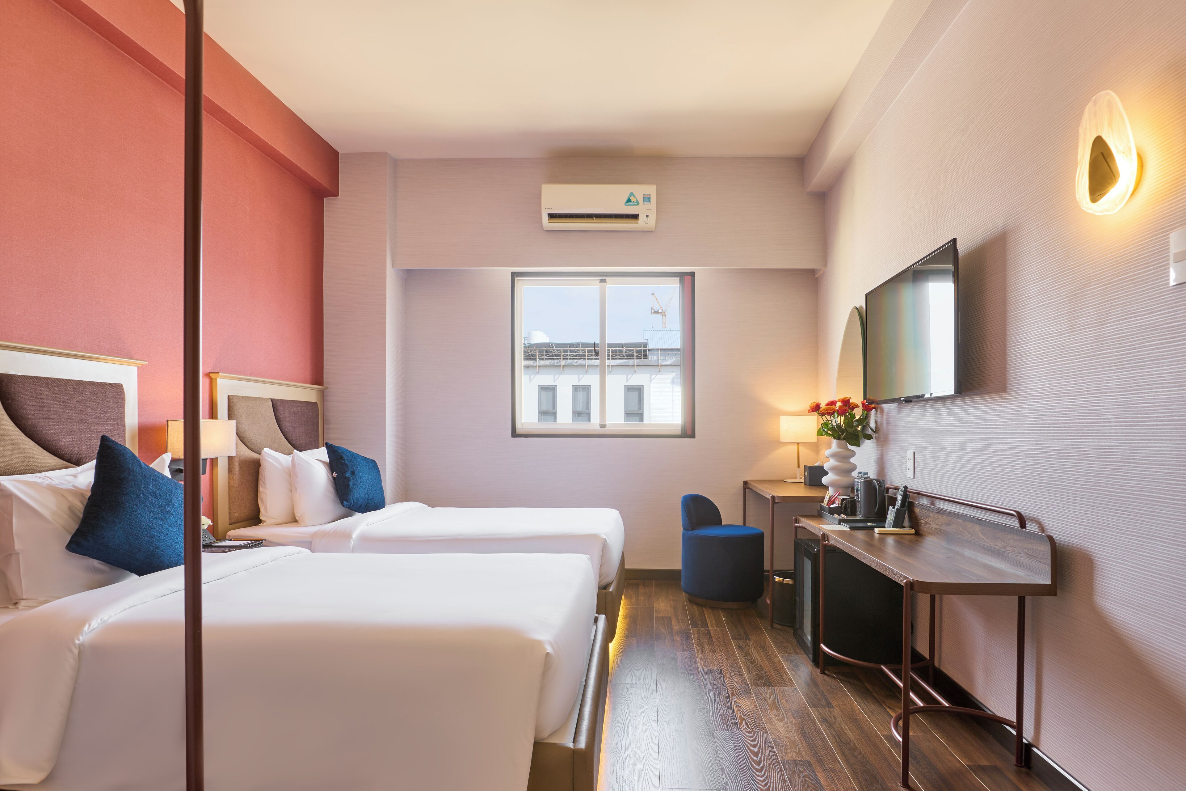 Habitación de hotel con dos camas, un escritorio, una silla, un televisor y un aire acondicionado.
