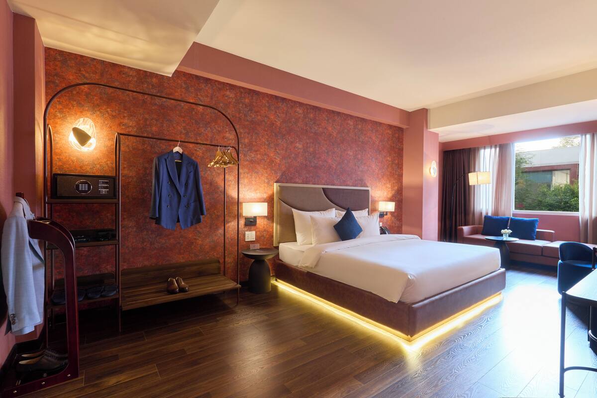 A hotel room with a large bed, a seating area, a shoe rack, and a desk.
