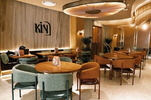 A modern hotel lobby with round tables, comfortable seating, and a prominent 'KIN' sign on the wall.