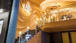 Entrada de hotel com fachada curva, um letreiro chamativo 'KIN HOTEL' e uma escadaria que leva ao andar superior.