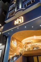 A hotel entrance with a curved facade, a prominent 'KIN HOTEL' sign, and a staircase leading to the upper floor.