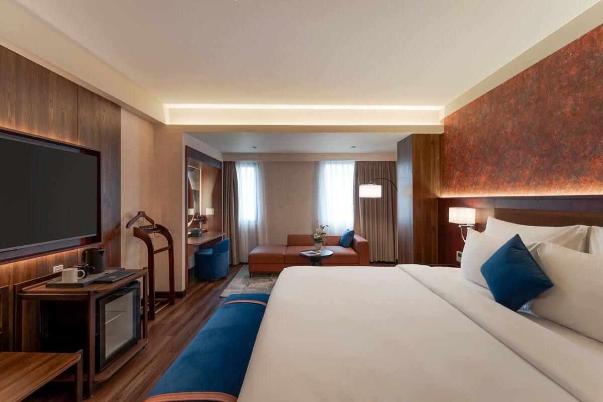 A hotel room with a large bed, a desk with a television, a sofa, and a lamp.