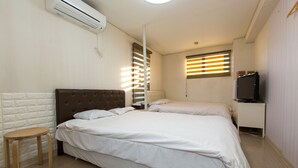 A bedroom with two beds, a small table, an air conditioning unit, a TV, and a window with blinds. - Hotel Empire in Shinjuku (Tokyo)