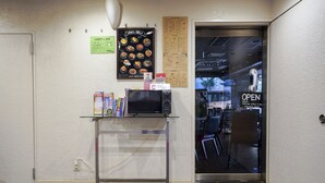 A clean, modern interior with a glass display case containing a microwave, books, and a small refrigerator. A menu board above the case lists various food items. - Hotel Empire in Shinjuku (Tokyo)