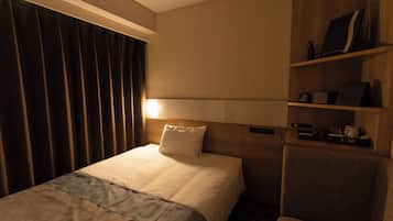Una camera d'albergo con un letto, un comodino, una sedia, uno scaffale con oggetti e una finestra con tende.