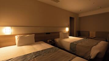 Ein Hotelzimmer mit zwei Betten, einem Nachttisch mit Lampe und einem Beistelltisch mit Telefon.