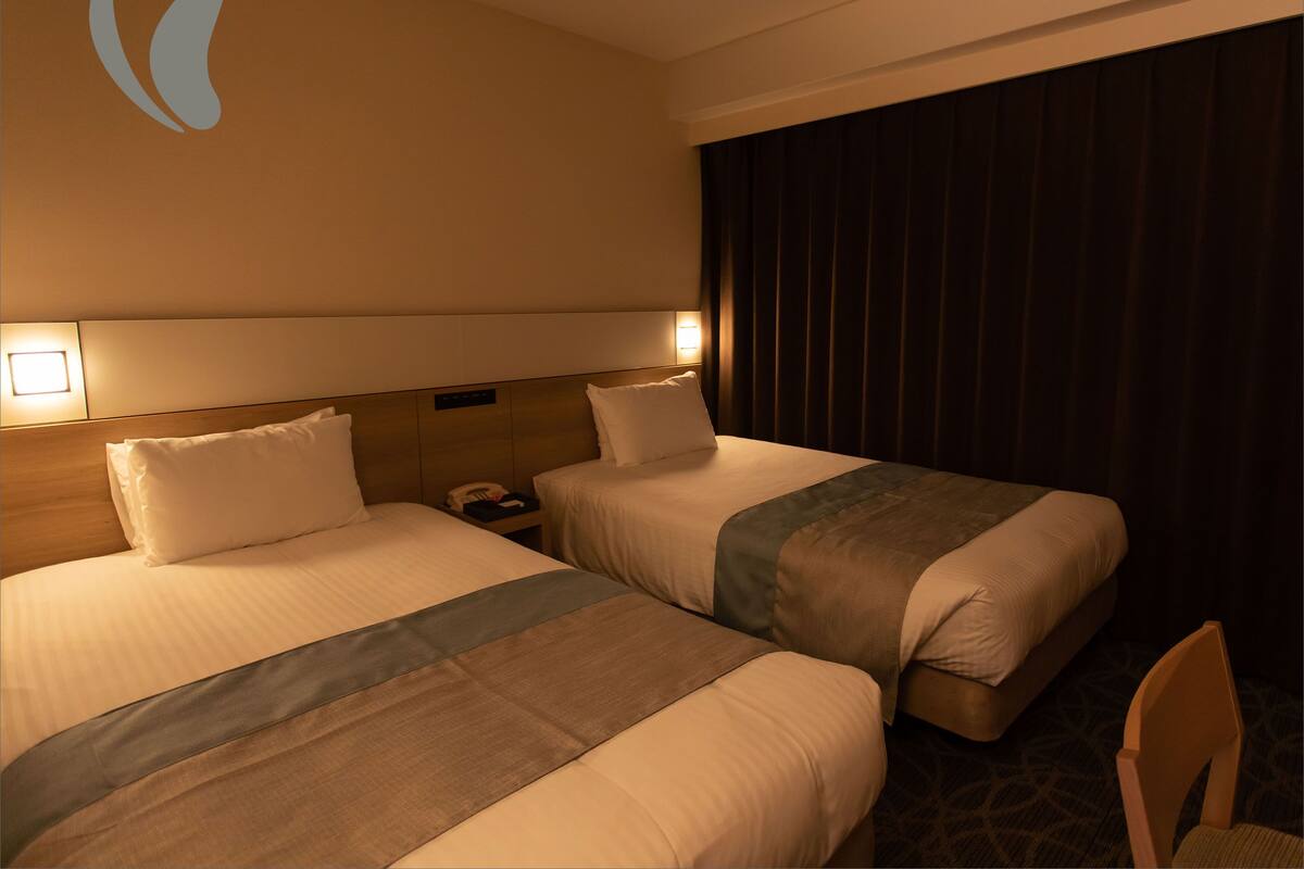 Een hotelkamer met twee bedden, een nachtkastje, een telefoon en een wandlamp.