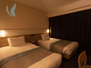Een hotelkamer met twee bedden, een nachtkastje, een telefoon en een wandlamp.