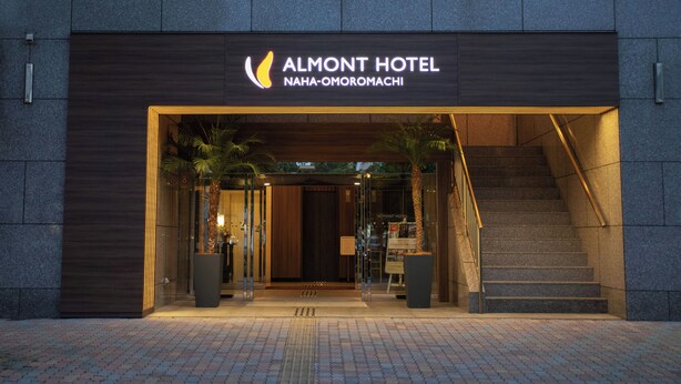 The exterior of the Almond Hotel with a modern design, featuring a prominent entrance, a staircase, and potted plants. - Almont Hotel Naha Omoromachi (Naha)