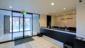A hotel reception area with a glass door entrance, a reception desk, and a wall sign that reads "Smile Hotel". - Smile Hotel Okinawa Naha (Naha)