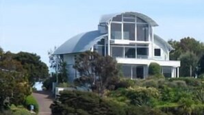 A modern two-story house with a large glass dome on the upper floor, surrounded by lush greenery. - Watermark Studio Apartments (Waiheke Island)