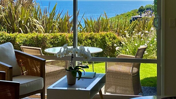 A balcony with a view of the sea, wicker furniture, and a small table with a plant. - Watermark Studio Apartments (Waiheke Island)