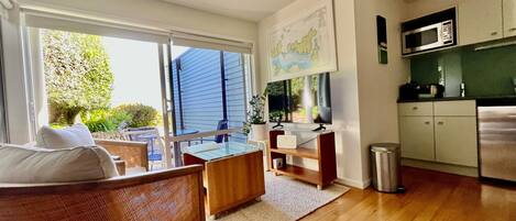 A modern living room with a large window, a flat-screen TV, a dining area, and a kitchen with a microwave.
