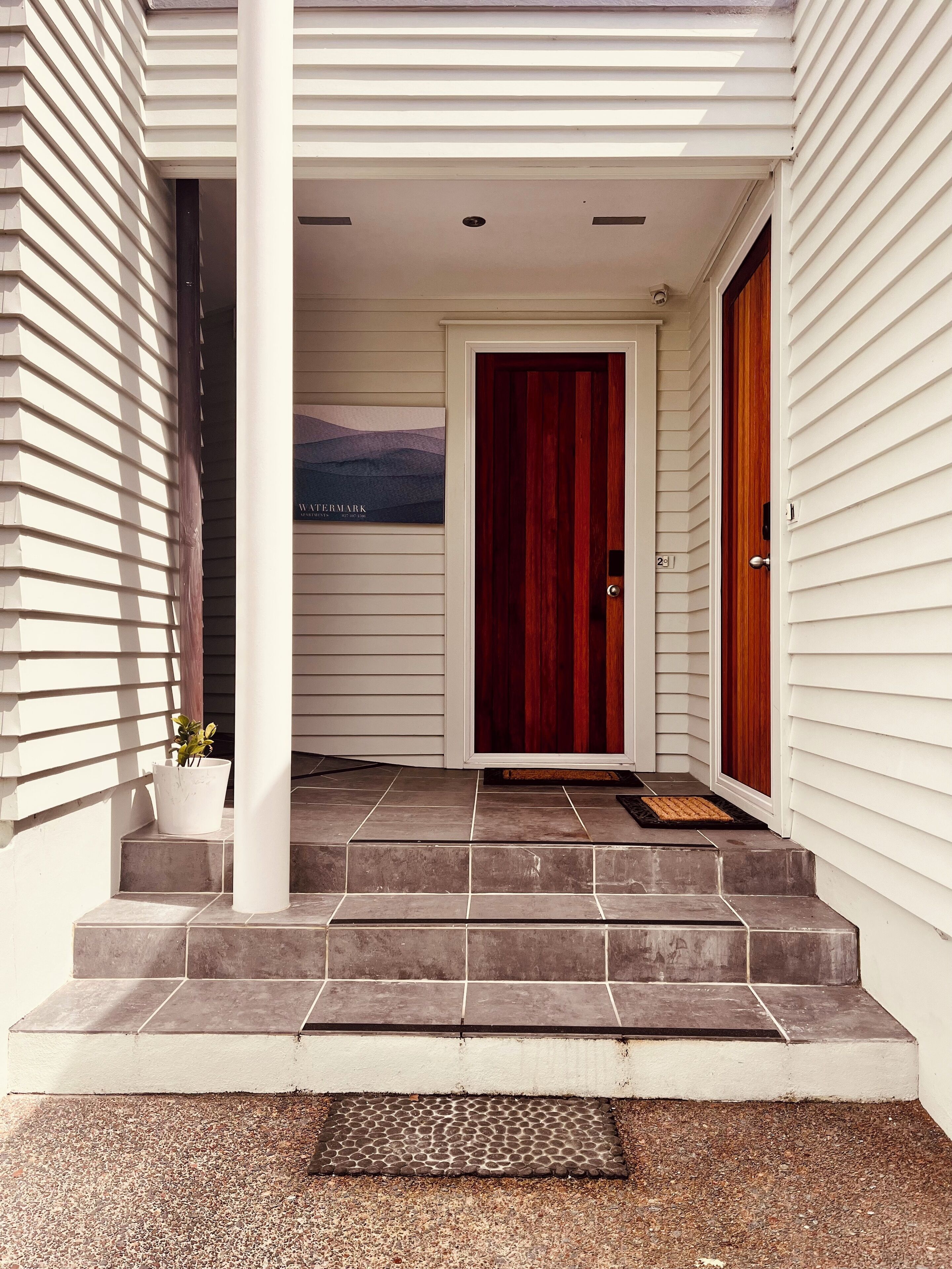 A house entrance with a red door, white siding, and a small potted plant on the steps.