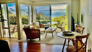 A modern living room with a large glass door leading to a balcony with a view of the sea. - Watermark Studio Apartments (Waiheke Island)