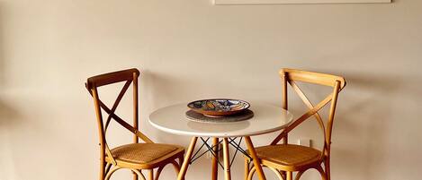 A dining area with a round table and two wooden chairs, a framed map on the wall, and a wooden floor.
