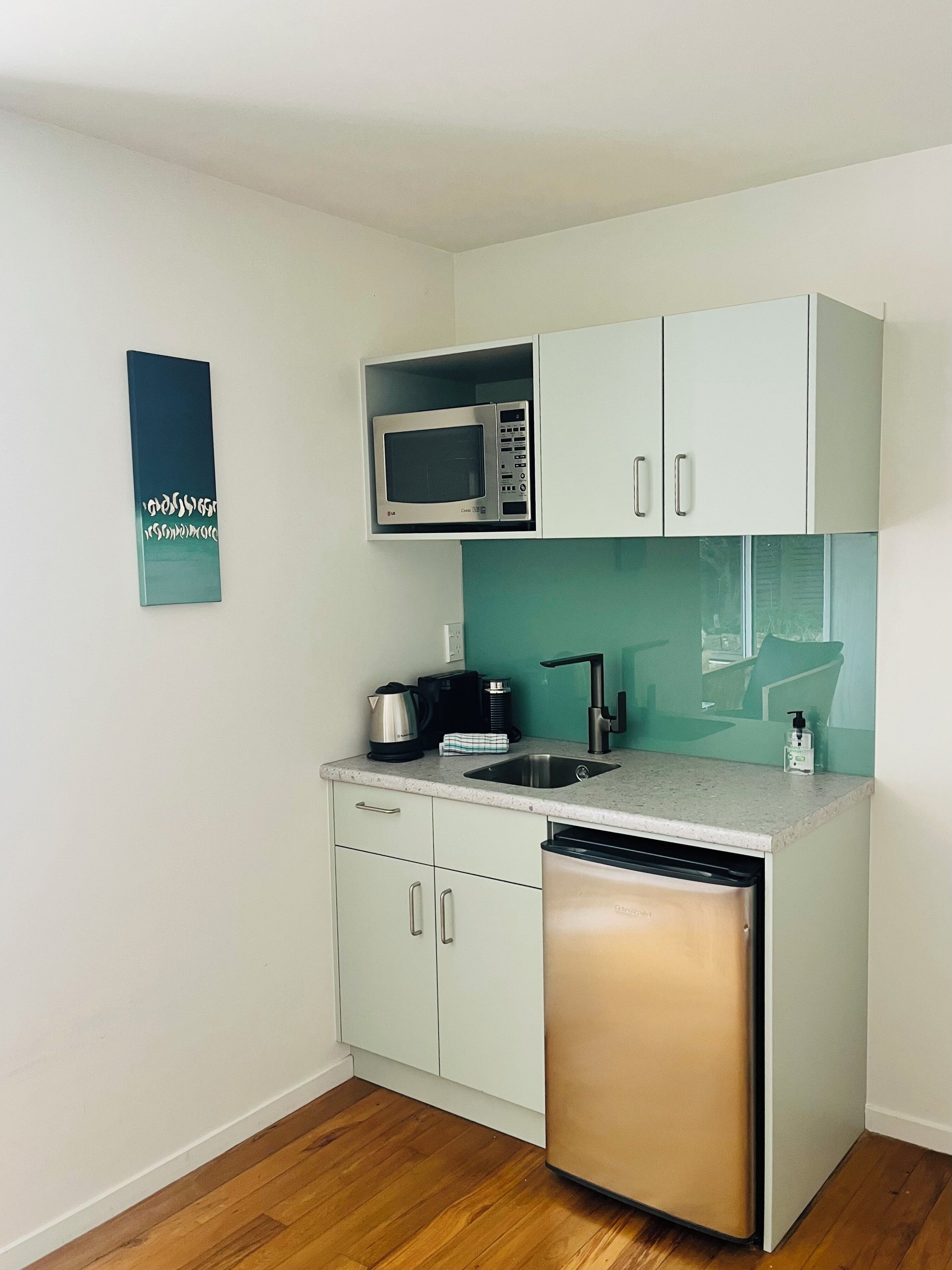 A compact kitchen with white cabinets, a stainless steel microwave, a coffee maker, and a dishwasher.