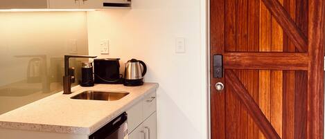 A compact kitchen with white cabinets, a stainless steel dishwasher, a microwave, and a coffee maker.