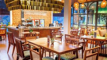 A restaurant interior with wooden tables and chairs, a bar area, and large windows.
