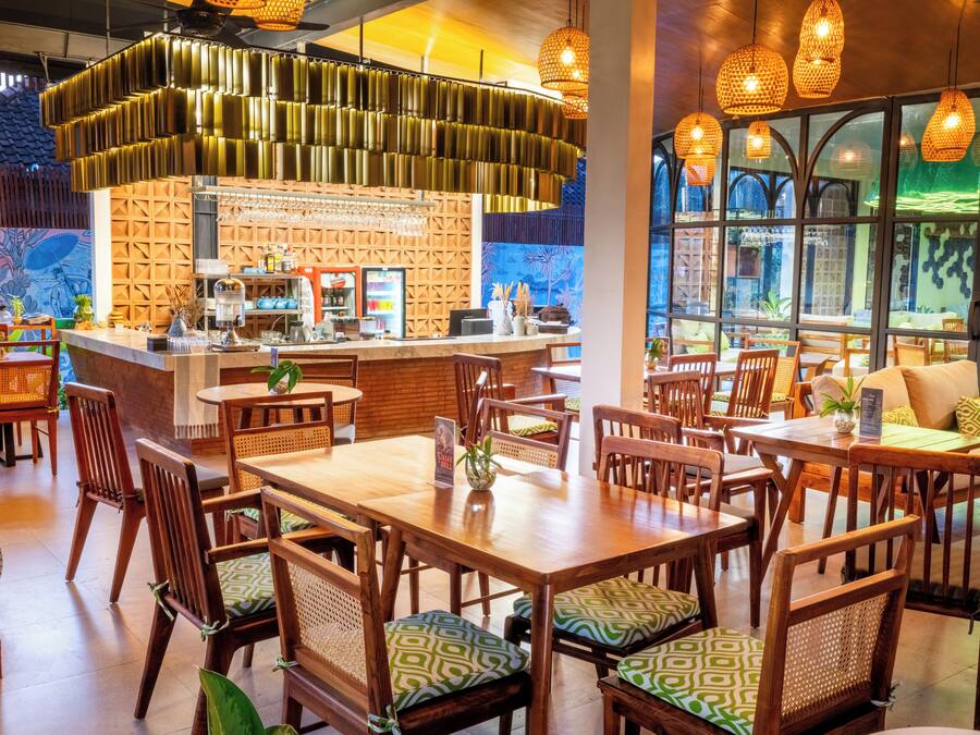 A restaurant interior with wooden tables and chairs, a bar area, and large windows.