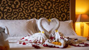 A bed with white linens and a heart-shaped towel arrangement with flowers.