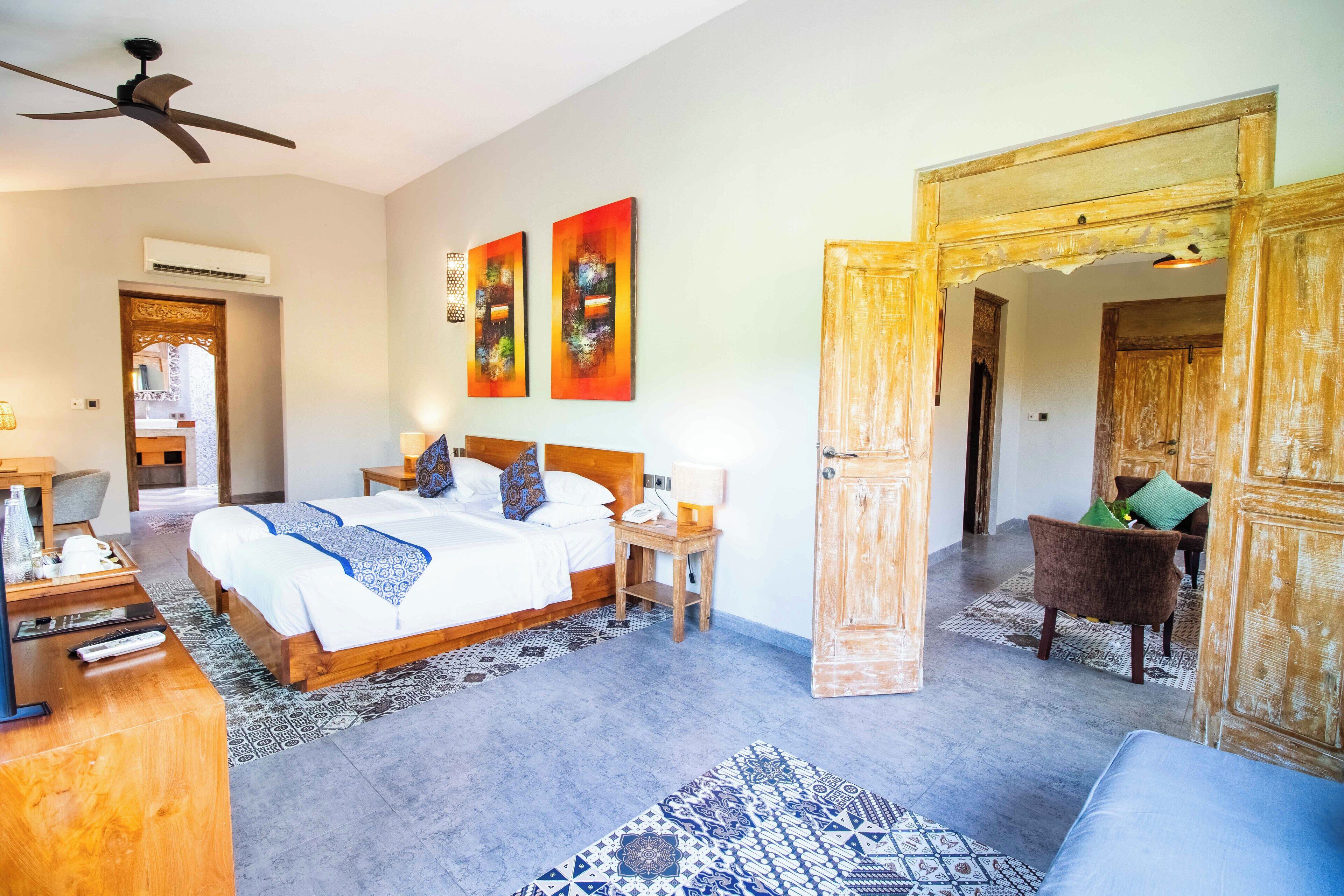 A hotel room with a large bed, a desk with a chair, a ceiling fan, and artwork on the wall.