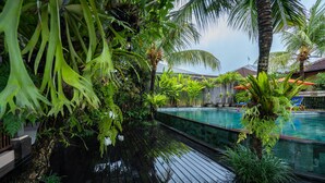 A poolside area with a wooden deck, lush greenery, and a clear pool. - Natya Hotel Tanah Lot (Tabanan)