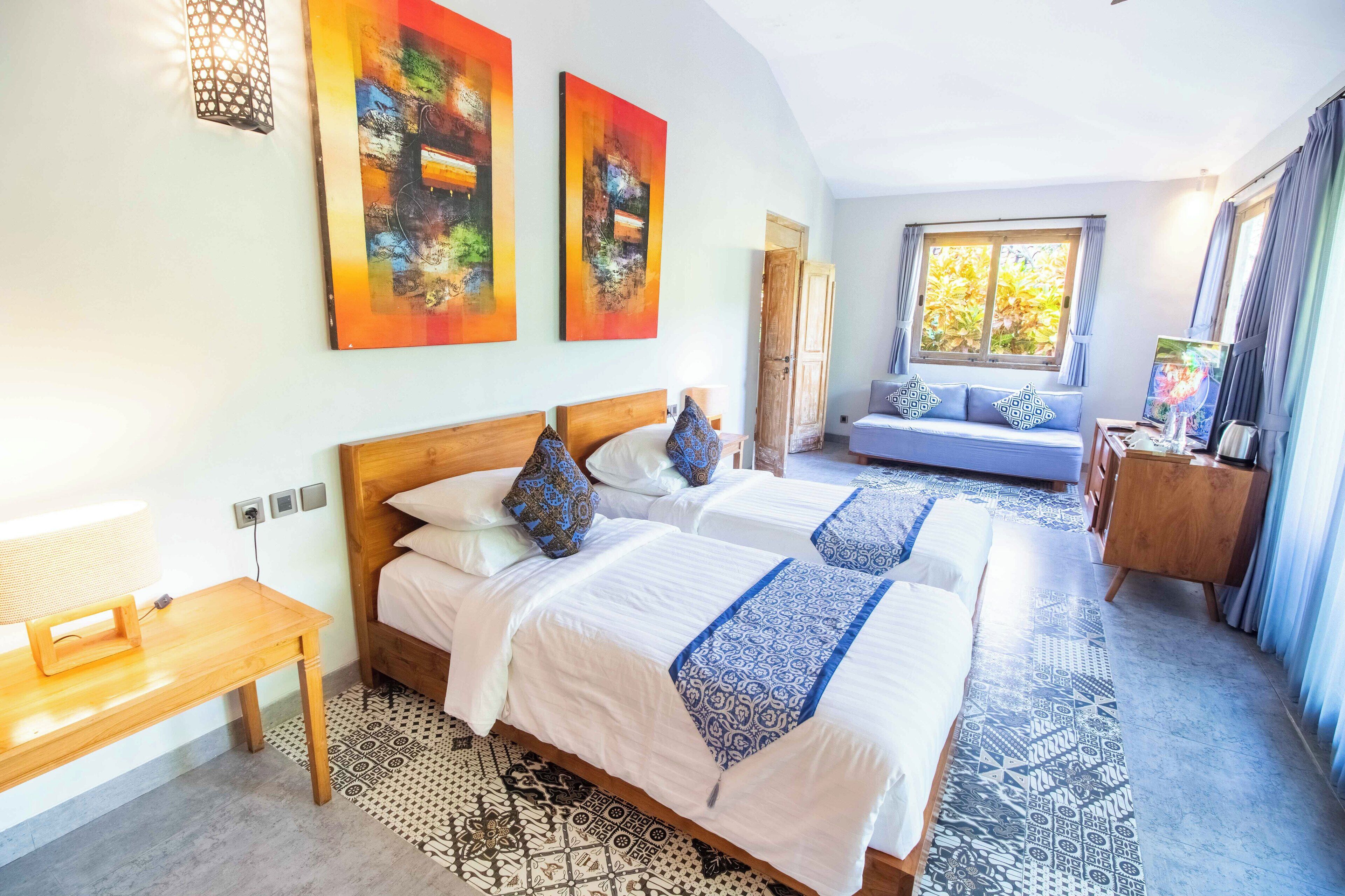 Habitación de hotel con dos camas, cabecero de madera, alfombra estampada y obras de arte en las paredes.