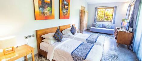 A hotel room with two beds, a wooden headboard, a patterned rug, and artwork on the walls.
