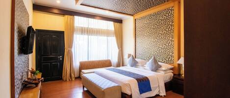 A hotel room with a large bed, a bench, a TV, and a window with curtains.