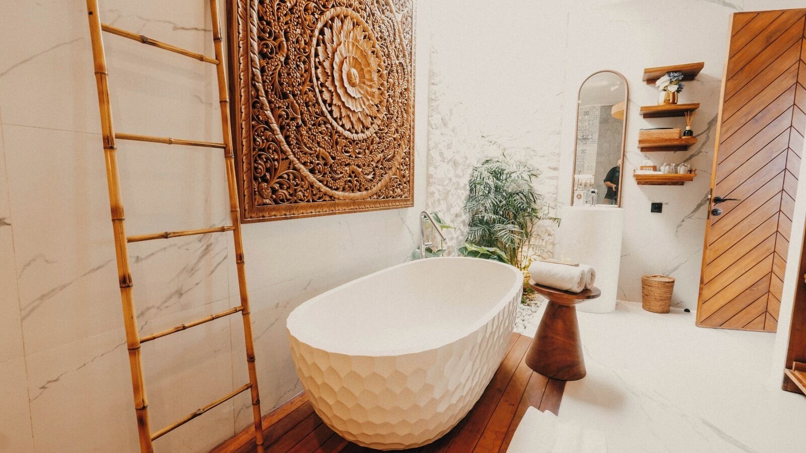 A modern bathroom with a freestanding bathtub, a decorative wall piece, and a wooden door.