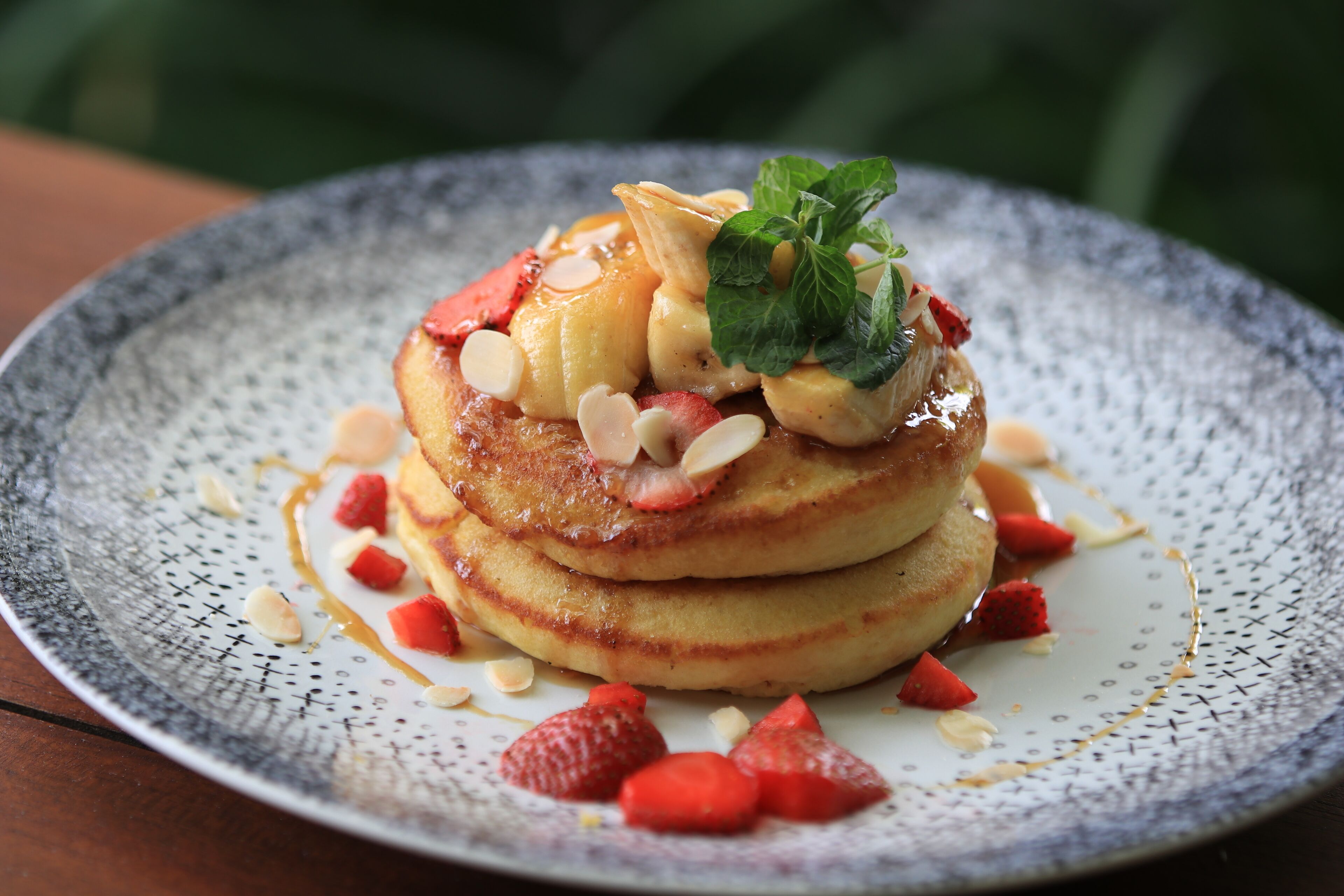 A stack of pancakes with fruit and nuts on a plate.