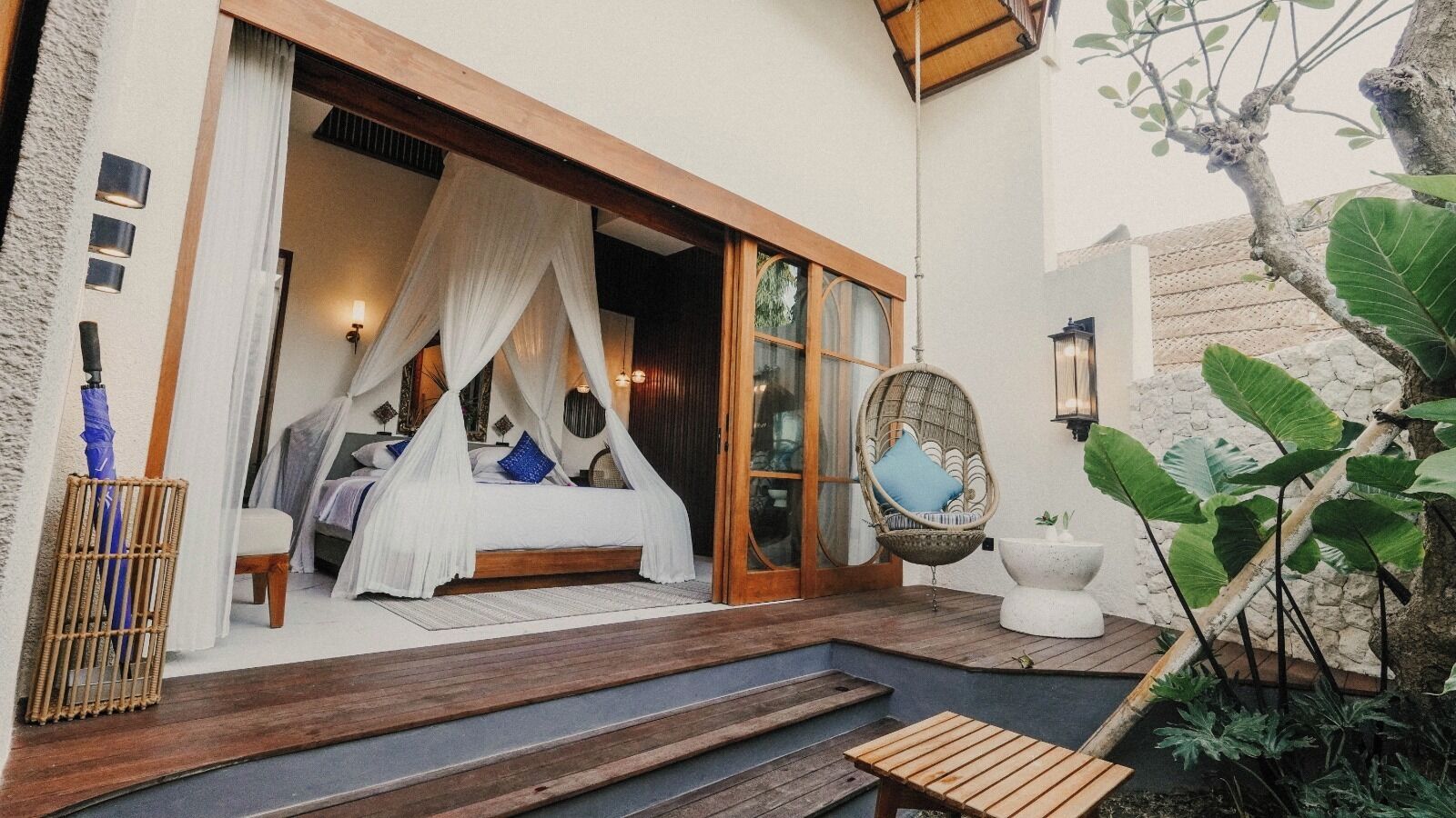 A bedroom with a canopy bed, a wicker chair, and a white pedestal.