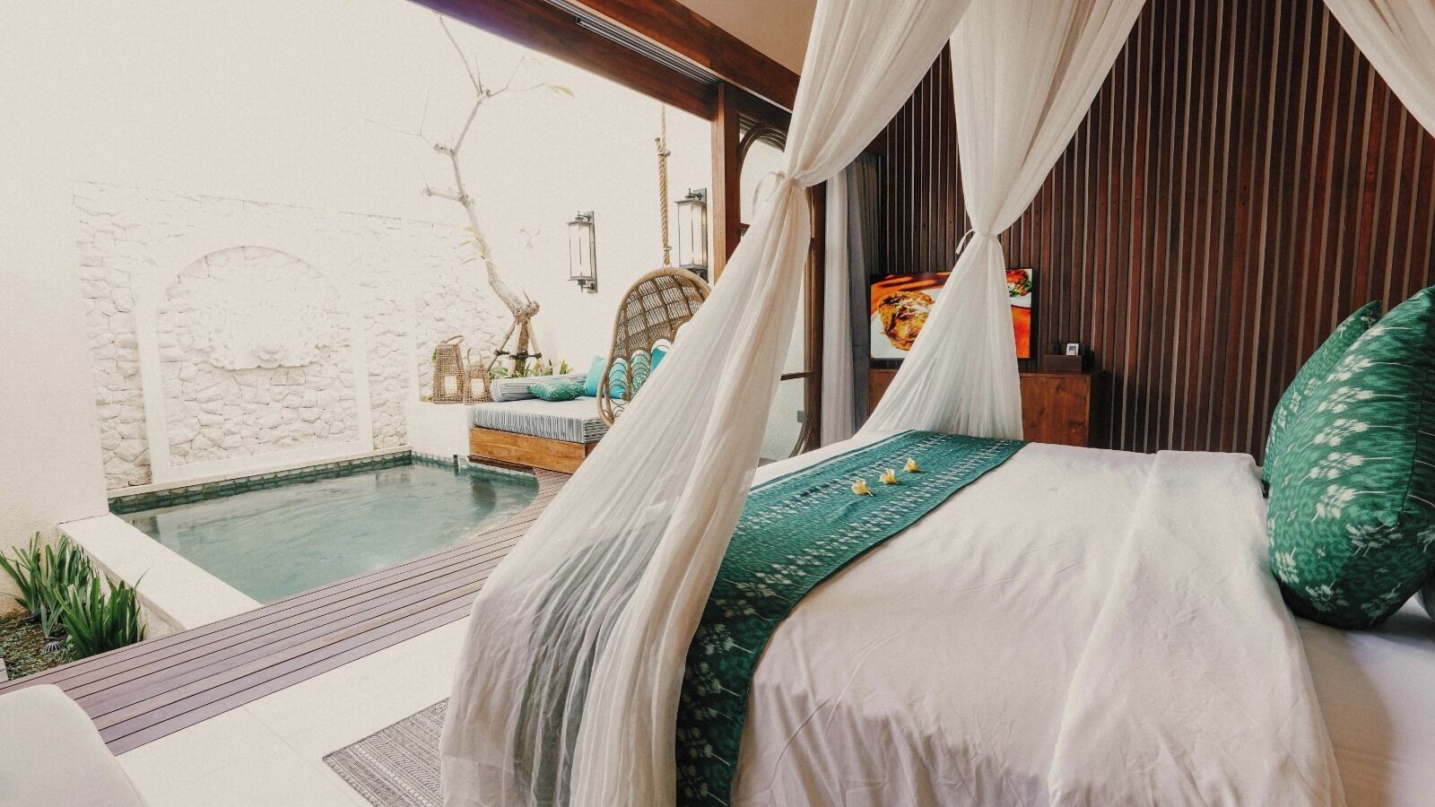 Un dormitorio con cama, dosel, vista a una piscina exterior y pared de piedra.