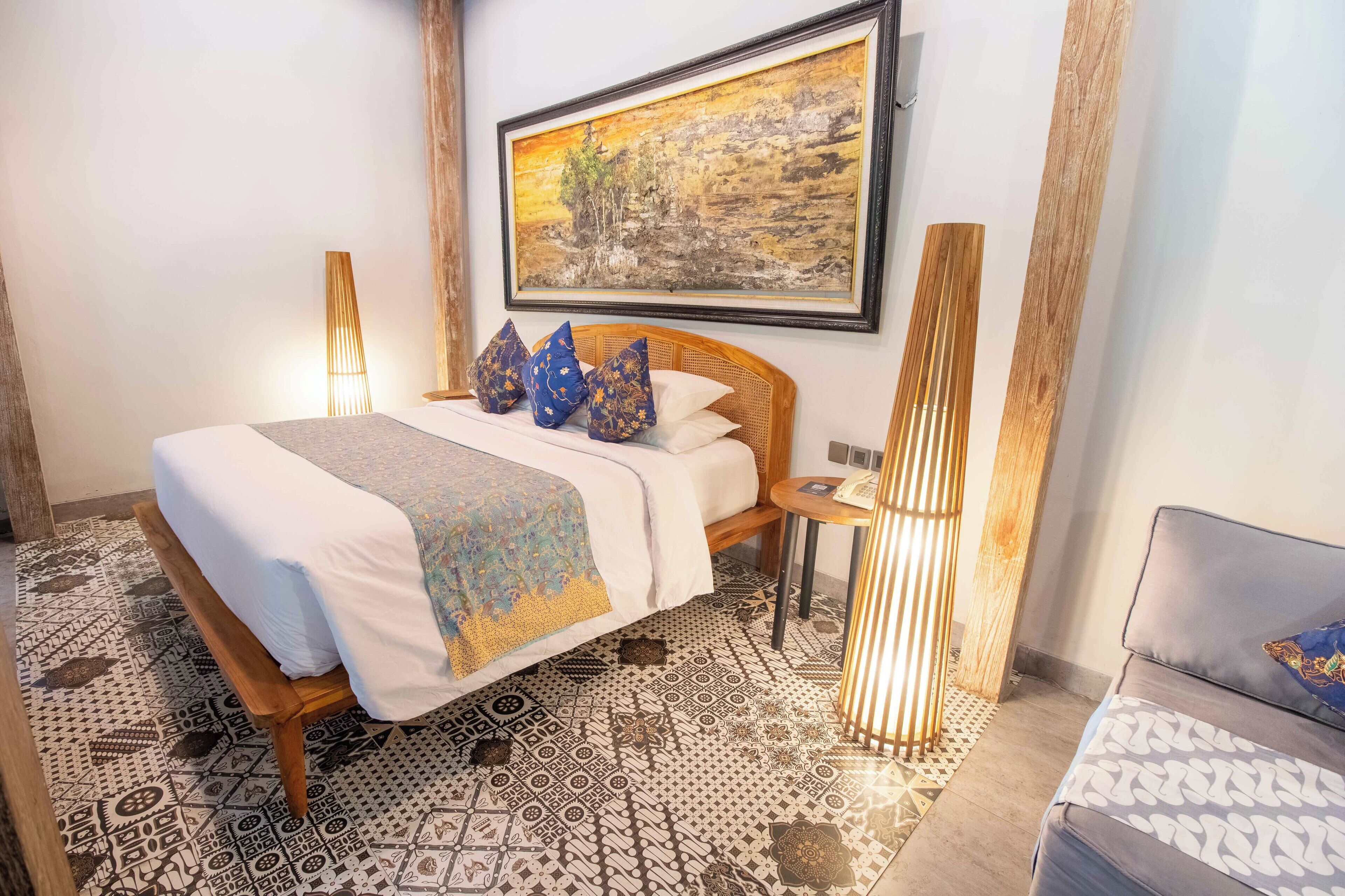 A neatly arranged bedroom with a bed, bedside tables, and a painting on the wall.
