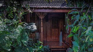 A traditional wooden house with a porch, surrounded by lush greenery. - Natya Hotel Tanah Lot (Tabanan)