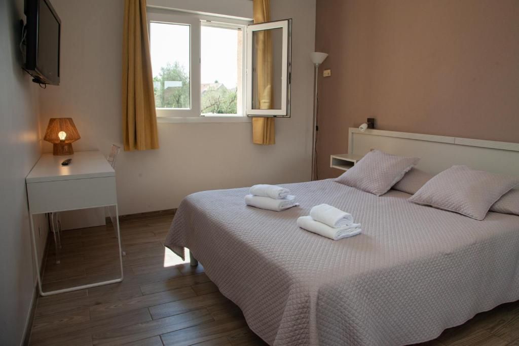 Quarto com cama, mesa de cabeceira com abajur, janela com cortinas e televisão na parede.