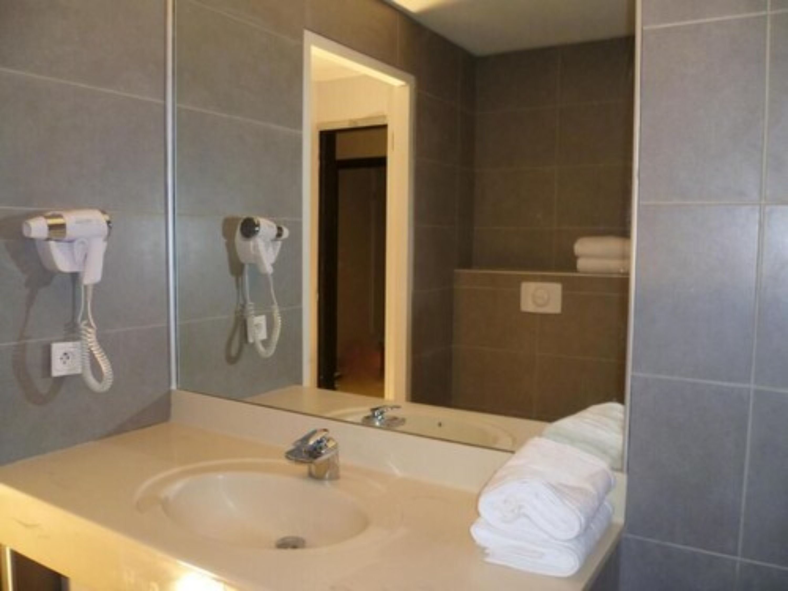 A bathroom with a sink, a mirror, and two hair dryers mounted on the wall.