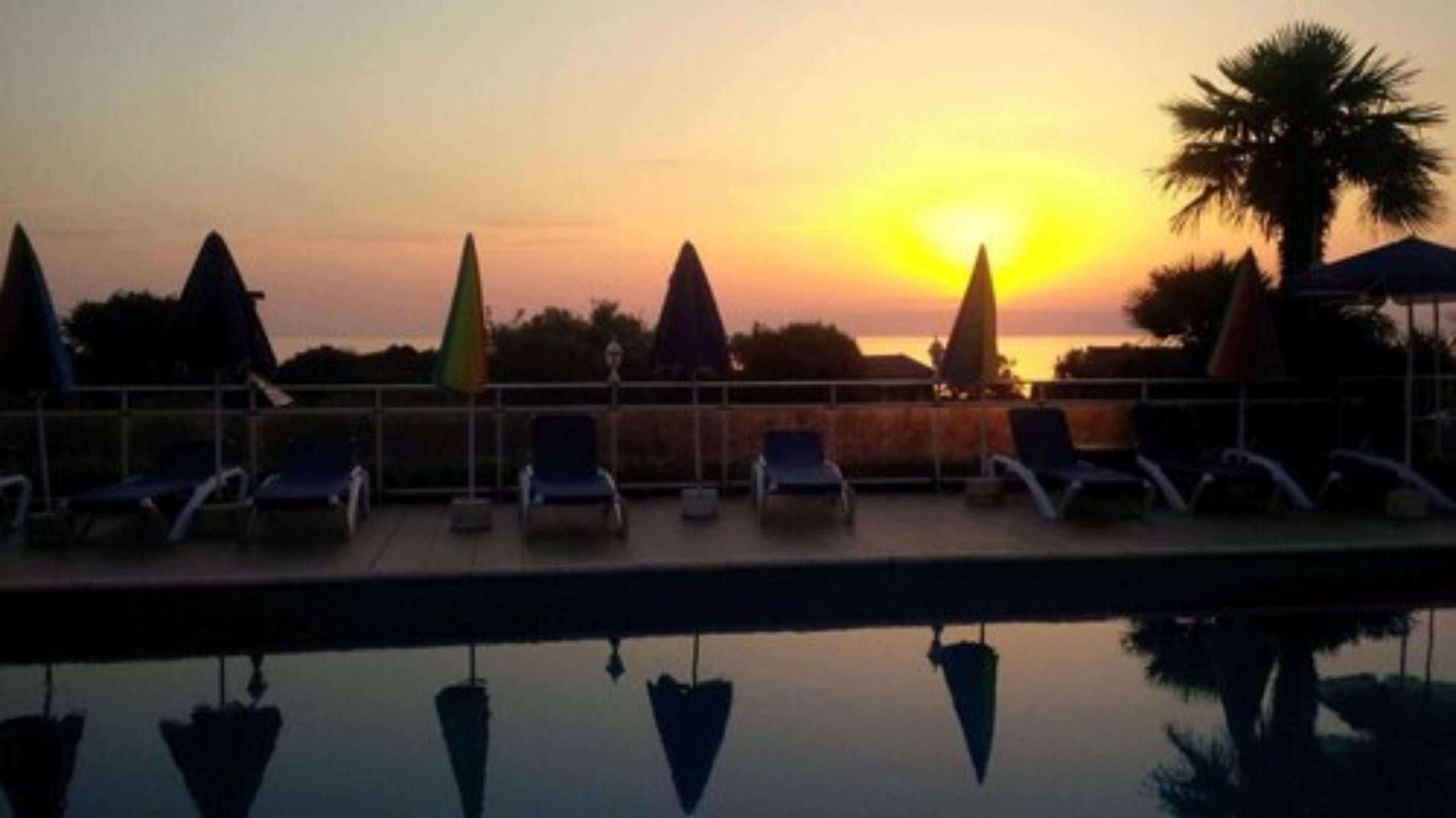 Un espace aménagé au bord de la piscine, avec des chaises longues et des parasols, au moment du coucher du soleil.