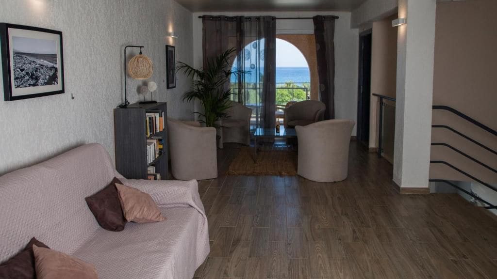 Un salón con sofá, una mesa de centro y una estantería. Se ve el exterior a través de una puerta de cristal.